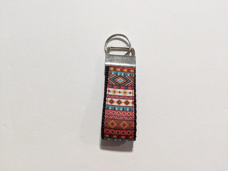 May include: A colorful key chain with a geometric pattern in shades of orange, red, blue, and white. The key chain has a silver metal ring and a black border.