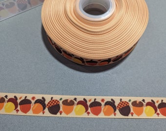 May include: A roll of beige ribbon with a repeating pattern of brown, orange, and yellow acorns. The ribbon is on a light blue surface.