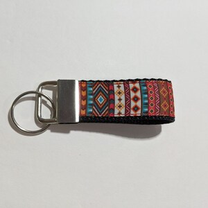 May include: A silver key chain with a black strap and a colorful geometric pattern. The pattern features red, orange, yellow, blue, and white colors.