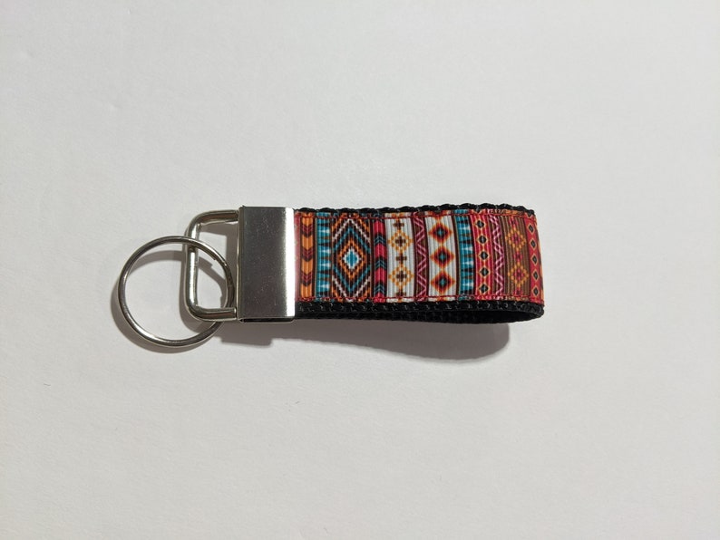 May include: A silver key chain with a black strap and a colorful geometric pattern. The pattern features red, orange, yellow, blue, and white colors.