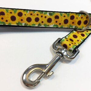May include: A black and yellow dog leash with a sunflower print and a silver clip.
