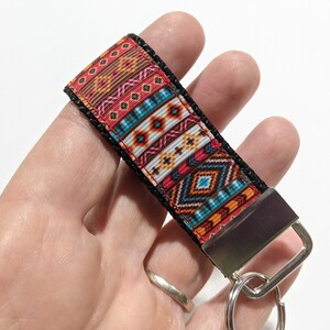 May include: A colorful key chain with a geometric pattern in shades of red, orange, blue, and white. The key chain has a black strap and a silver metal ring.