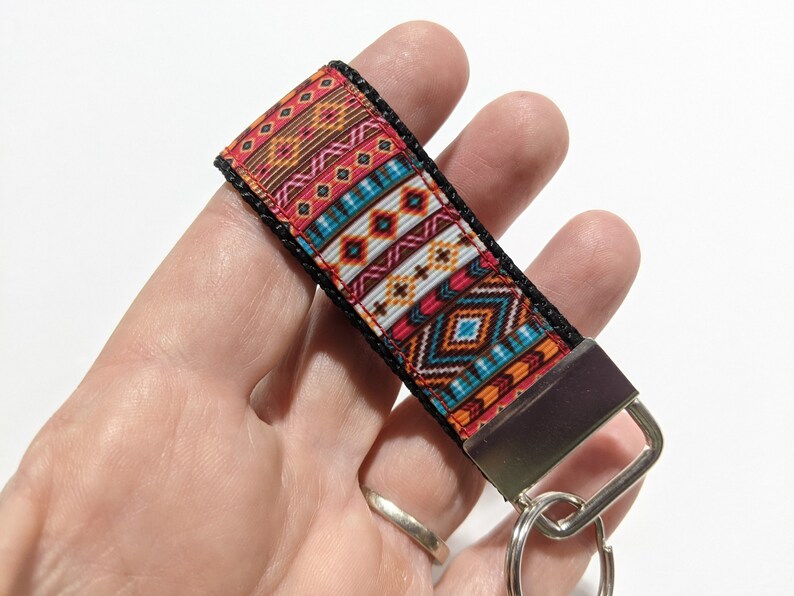 May include: A colorful key chain with a geometric pattern in shades of red, orange, blue, and white. The key chain has a black strap and a silver metal ring.