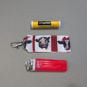 May include: A red and white cow print keychain with a silver clip. A yellow ChapStick tube with the text "ChapStick Original Lip Balm" and a red lighter with the text "Bic" are also pictured.
