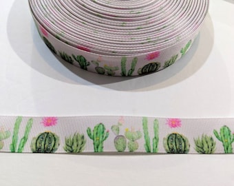 May include: White ribbon with a repeating pattern of green cacti and pink flowers. The ribbon is rolled up and the pattern is visible on the side of the roll.