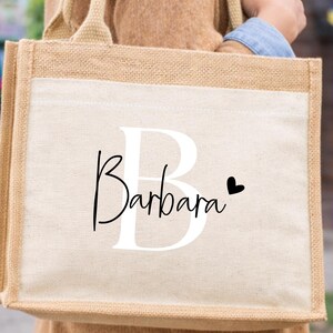 Op de afbeelding: Een beige draagtas met een wit voorpaneel. De naam "Barbara" is in cursief schrift geschreven met een grote witte "B" en een klein zwart hart. De tas heeft een "Bestseller" sticker.