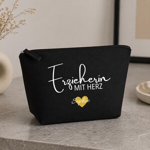 May include: Black cosmetic bag with a zip closure. The bag features the text "Erzieherin MIT HERZ" in white script, a gold heart, and the name "Sophie". The bag is on a grey surface.
