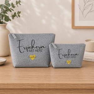 May include: Two grey felt zipper pouches. The larger pouch has the text "Erzieherin MIT HERZ Sophie" in black script with a yellow heart. The smaller pouch has the same text and design. Both pouches have silver zips.