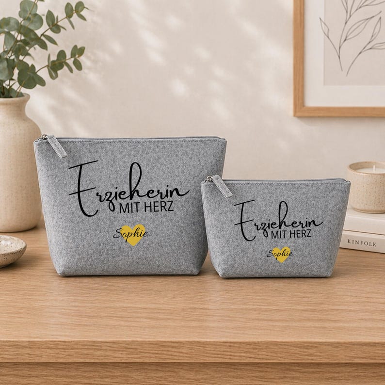 May include: Two grey felt zipper pouches. The larger pouch has the text "Erzieherin MIT HERZ Sophie" in black script with a yellow heart. The smaller pouch has the same text and design. Both pouches have silver zips.
