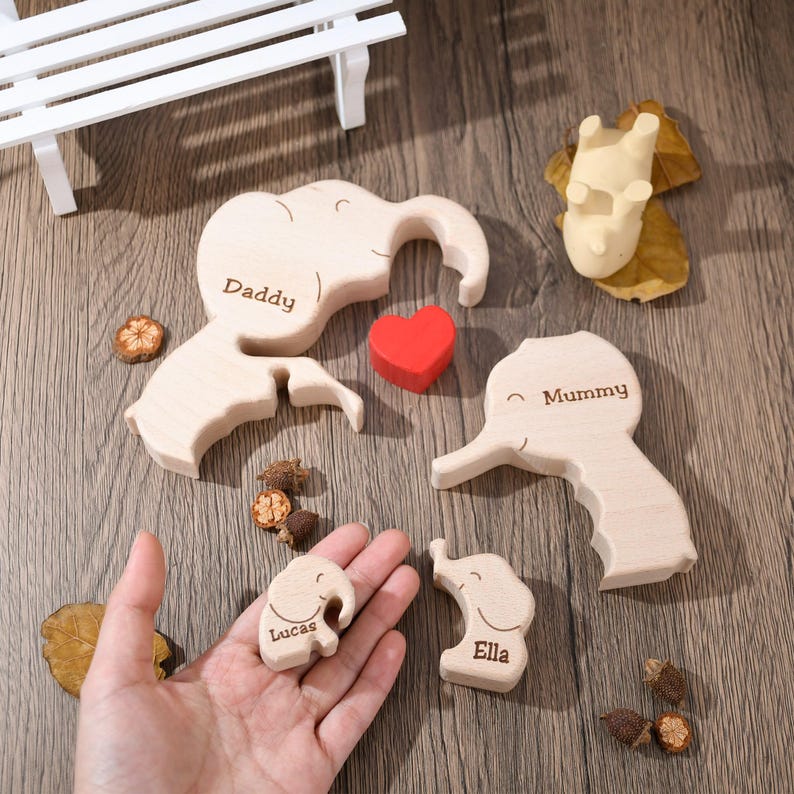 K&ouml;nnte beinhalten: Holzpuzzle einer Elefantenfamilie mit den Namen "Daddy", "Mummy", "Lucas" und "Ella", die auf jedes Teil graviert sind. Ein rotes Herz ist im Puzzle enthalten.