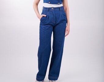 May include: A denim two-piece outfit featuring a sleeveless top with gold buttons and wide-leg pants. The top has a double-breasted design. The outfit is a deep blue color and is paired with white sneakers.
