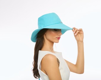 May include: A light blue sun hat with a wide brim. The hat has a simple design with a small decorative element on the band. The brim is slightly curved, and the hat is being held up by a person.