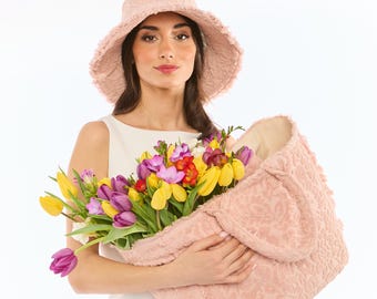 May include: A woman wearing a pink hat holds a pink fuzzy tote bag filled with a bouquet of colorful tulips and other flowers.