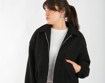 May include: A black cropped fleece jacket with a zipper closure and a collar. The jacket has a slightly oversized fit and is made of a soft, fuzzy material.