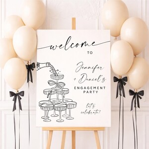 May include: A white engagement party sign on an easel, with the words "welcome to Jennifer + Daniel's Engagement Party" in black script. Champagne glasses are illustrated below the text. Cream-colored balloons and black bows decorate the scene.