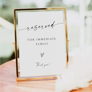 Könnte beinhalten: Ein goldgerahmtes Schild mit dem Wort "reserved" in eleganter Schrift. Das Schild enthält auch den Text "FOR IMMEDIATE FAMILY", ein Herzsymbol und "Thank you!" in einer zarten Schriftart. Das Schild wird auf einer Holzoberfläche angezeigt.