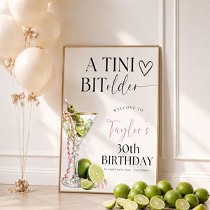 May include: A rectangular birthday sign with the text A TINI BIT older, Welcome to Taylor's 30th BIRTHDAY, and So Glad You're Here - Let's Party! The sign features a martini glass with olives, pearls, and limes, next to cream-coloured balloons.