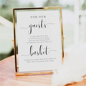 Könnte beinhalten: Ein goldgerahmtes Schild mit dem Text "FOR OUR guests" in eleganter Schrift. Das Schild enthält Anweisungen und das Wort "basket" in ähnlicher Schrift. Das Schild ist für eine Hochzeit oder Veranstaltung gedacht.