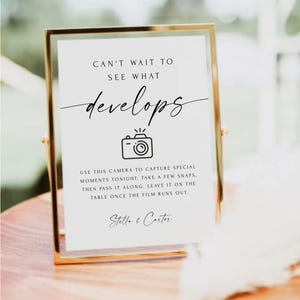 May include: A gold-framed sign with a white background and black text that reads "Can't wait to see what develops."  A black and white illustration of a camera is below the text. The sign also includes the text "Use this camera to capture special moments tonight. Take a few snaps. Then pass it along. Leave it on the table once the film runs out." and "Stella & Carter."