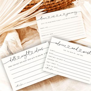 May include: Three white cards with black script, designed for a wedding. The cards have lines for writing and feature phrases like "love is a journey" and "advice and wish." The cards are decorated with hearts.