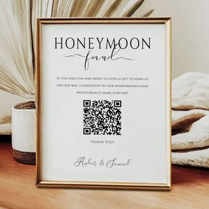 Könnte beinhalten: Ein weißes Schild mit goldenem Rahmen, auf dem "Honeymoon Fund" in einer dekorativen Schreibschrift steht. Das Schild hat einen QR-Code und den Text "Wenn Sie Spaß hatten und ein Geschenk geben möchten, um uns auf den Weg zu schicken, wäre eine Spende für unseren Flitterwochenfonds wirklich ein Traum! Danke! Amber & Samuel"