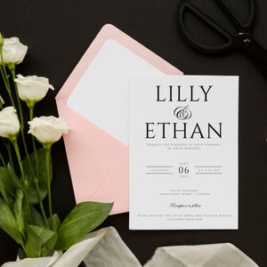 May include: A white wedding invitation with black text. The invitation reads "Lilly & Ethan" and includes the date and time of the wedding, the location, and the RSVP information.