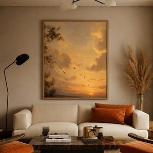 May include: A large square framed wall art piece depicting a sunset landscape with golden clouds and birds in flight, positioned above a cream-coloured sofa with orange throw pillows, a dark marble coffee table, and two orange armchairs.