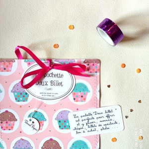 Könnte beinhalten: Eine rosa Geschenkverpackung mit Cupcake-Motiv, rosa Schleife, einer Rolle lila Glitzertape und orangefarbenem Konfetti. Die Tasche hat ein Etikett mit "pochette Doux Billet" und eine handschriftliche Notiz.
