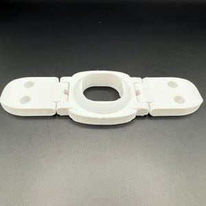 May include: A white, hinged, 3D-printed object with a central circular opening and two rectangular end pieces, each with two circular indentations. The object is designed to be folded.