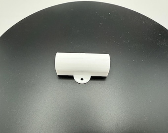 May include: A white, cylindrical, 3D-printed plastic component featuring a flat, protruding tab with a single circular hole centered along the bottom edge. The object has a smooth, matte finish and a hollow, open-ended tubular structure.