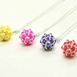 Puede incluir: Cuatro collares de bolas de papel origami con cadenas plateadas. Las bolas son blancas con patrones geométricos y son de color amarillo, rosa, morado y rojo.