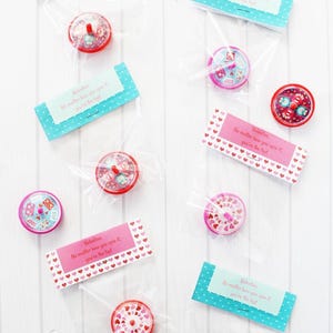 May include: A set of eight Valentine's Day party favors, each containing a small spinning top with a heart design. The tops are packaged in clear plastic bags with colorful tags that read "Valentine. No matter how you spin it, you're the top!"
