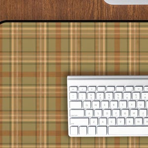 Könnte beinhalten: Ein Computer-Setup mit weißer Tastatur, Maus und einer karierten Mausunterlage in Grün-, Braun- und Beigetönen. Das Setup befindet sich auf einem Holzschreibtisch, mit einem Computermonitor darüber.