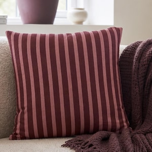 Può includere: Interno di un soggiorno con un divano color crema, un cuscino a righe bordeaux e una coperta abbinata. Un tavolino in legno con una tazza e una piccola ciotola. Elementi decorativi: vaso e opera d'arte incorniciata.