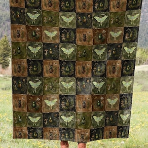 May include: A large, square blanket featuring a repeating pattern of insects and moths in shades of green, brown, and black. The blanket is displayed in a field with a mountain backdrop, highlighting its design and size.