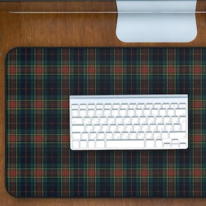 May include: A desk setup featuring a plaid patterned mousepad in shades of green, red, and navy blue. A white keyboard sits on the pad, with a computer monitor above. A small potted plant and a coffee cup are also visible.