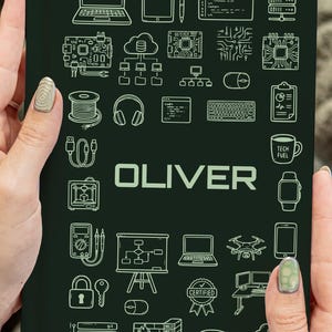 Peut inclure: Un cahier vert foncé avec des illustrations blanches de symboles technologiques, tels que des ordinateurs portables, des serveurs et un drone. Le nom "OLIVER" est imprimé en blanc. Le cahier est tenu par une personne.