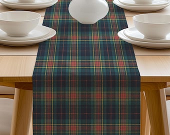 May include: A dining table set with a plaid table runner in shades of navy, green, red, and yellow. The table is set with white bowls and plates, a white vase with dried flowers, and wooden chairs.