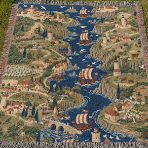 Könnte beinhalten: Eine rechteckige, gewebte Wandteppichdecke mit einer detaillierten Küstenlandschaft, einem zentralen blauen Wasserweg, mehreren Segelschiffen, Leuchttürmen, Steinbrücken und kleinen Dorfhäusern inmitten grüner Hügel und felsiger Klippen.