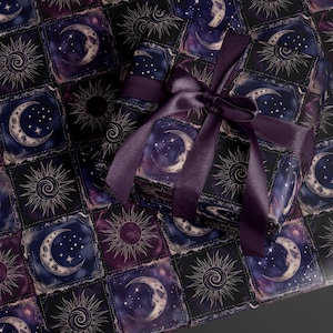 May include: A rectangular gift box wrapped in dark purple and black paper featuring a repeating grid pattern of celestial sun and moon illustrations, tied with a wide, smooth, dark purple satin ribbon bow centred on the top surface.