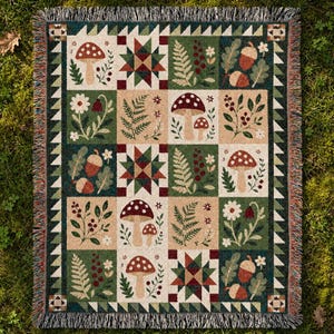 Puede incluir: Una manta tejida con un patrón de cuadrícula de ilustraciones botánicas que incluyen setas, helechos, bellotas y motivos de estrellas en tonos verde bosque, crema y rojo oscuro, con un borde decorativo de flecos en los cuatro lados.