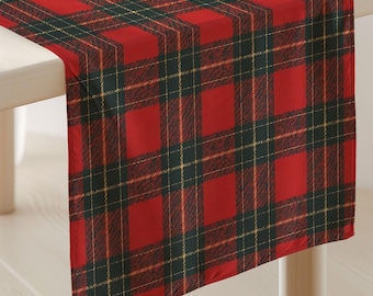 Pode incluir: Um caminho de mesa xadrez vermelho e preto com um padrão repetitivo. O caminho de mesa é drapeado sobre uma mesa branca, com uma chaleira, uma xícara e um vaso brancos ao fundo. O design xadrez apresenta uma grade de quadrados vermelhos e pretos com finas linhas douradas.