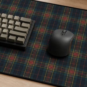 May include: A rectangular desk mat featuring a dark green, navy blue, and red plaid pattern with a black stitched border. A compact mechanical keyboard with light gray keycaps and a dark gray wireless computer mouse are placed on the mat.