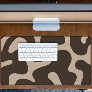May include: A desk setup with a white keyboard on a brown and beige patterned mousepad. The desk also includes a monitor, a wooden tray with small plants, and a wooden surface.