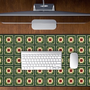 May include: A rectangular mouse pad with a floral pattern in green, red, and cream colors. A white keyboard and mouse are on the pad. The pad is on a wooden surface, with a computer monitor above.