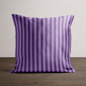 May include: A square decorative pillow with vertical stripes in shades of purple. The pillow is resting on a dark wooden surface. The stripes alternate between light and dark purple.