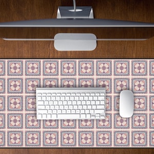 May include: A computer setup featuring a patterned mousepad with a floral design in shades of pink, purple, and cream. A white keyboard and mouse are positioned on the pad. The setup is on a wooden desk, with a computer monitor above.