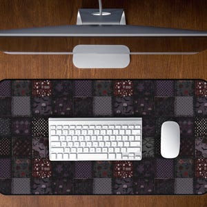 May include: A rectangular mouse pad with a patchwork design featuring skulls, bats, and floral patterns in shades of gray, purple, and burgundy. A white keyboard and mouse are on the pad. A computer monitor is above.