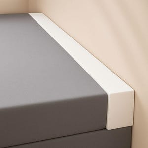 May include: Close-up of a grey, rectangular surface with a white border. The white border is on the top and side of the grey surface. The background is a light beige colour.