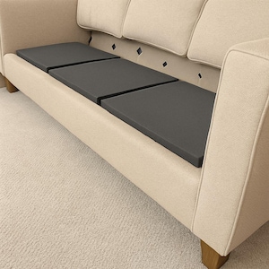 May include: A beige upholstered sofa with three dark gray seat cushions. The sofa has a high back with three cushions and wooden legs. The background is a light beige carpet.